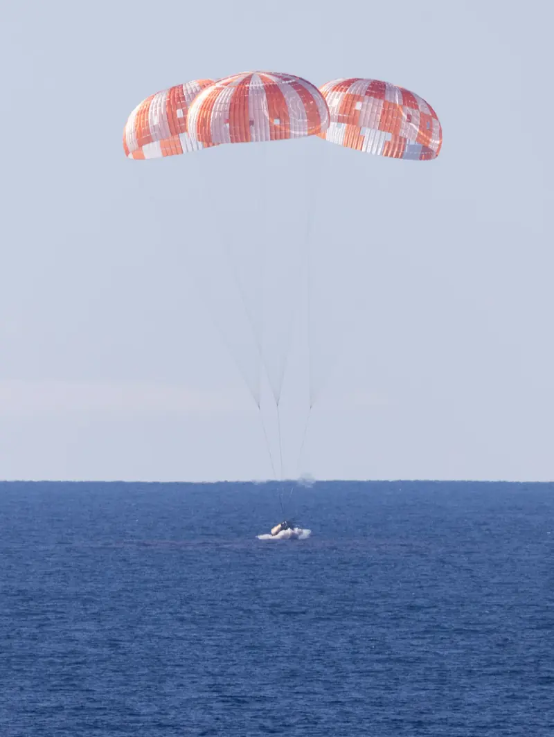 Three orange-and-white parachutes against the sky during Artemis II's return